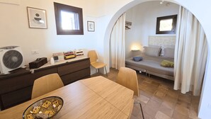 A compact room with a bed, a desk, a chair, a table, and a fan. - Dammuso - Cala Cinque Denti - AFFITTI\'CA (Pantelleria)