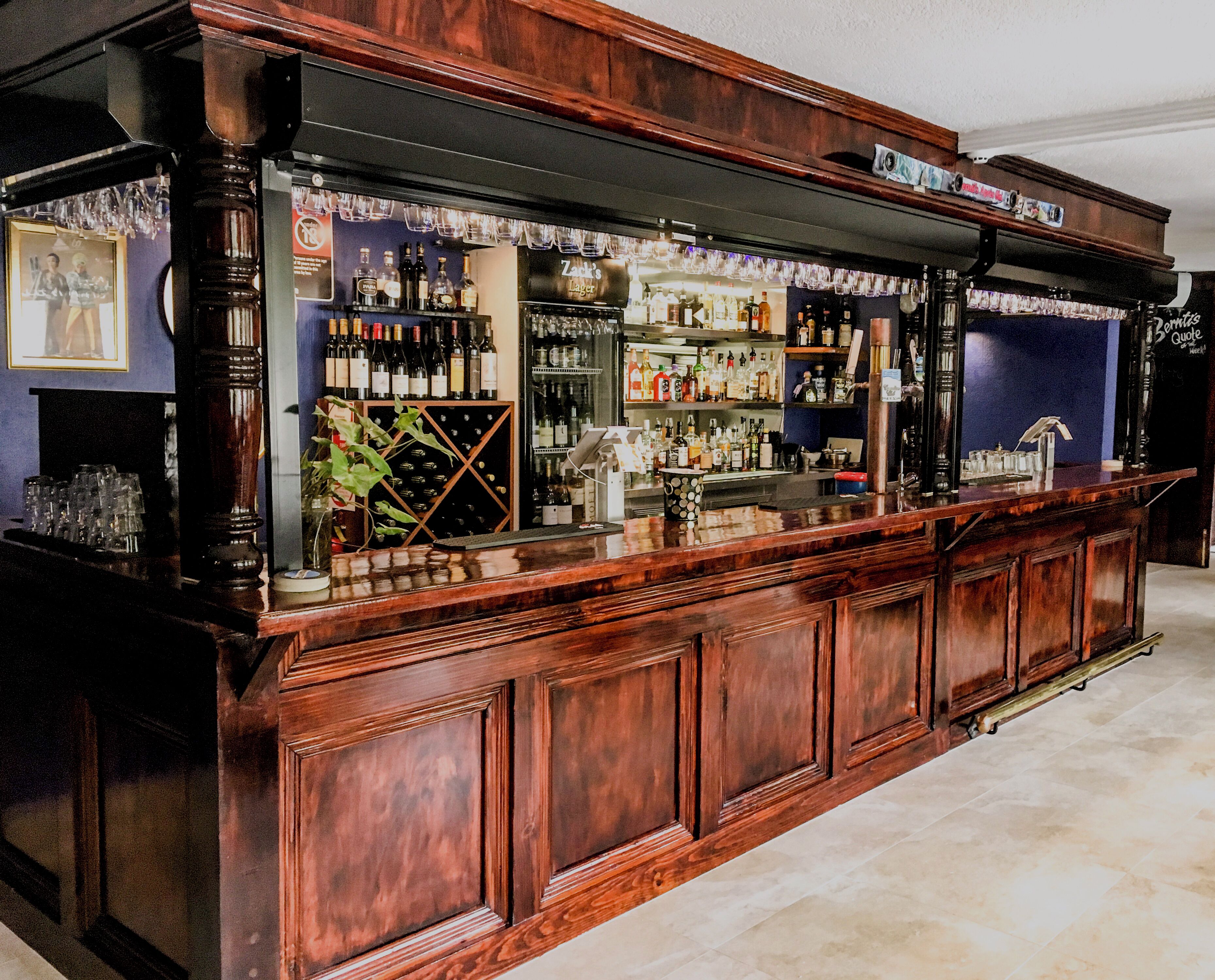 A bar area with a wooden counter, shelves of liquor bottles, and a wine rack.