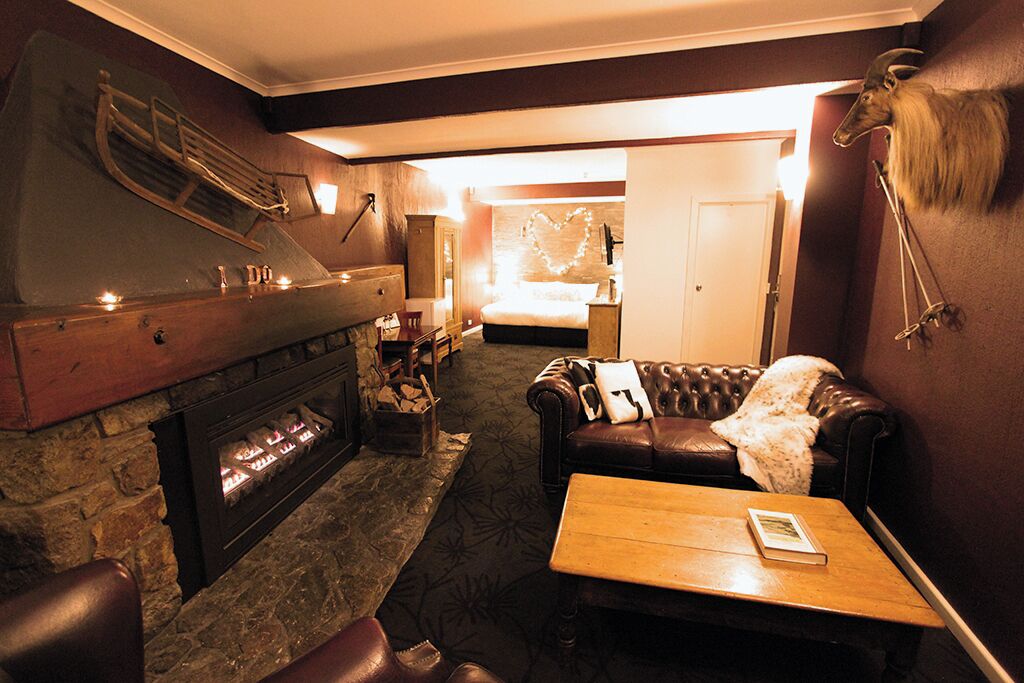 A cozy room with a fireplace, leather sofa, and a bed with a heart-shaped light decoration.