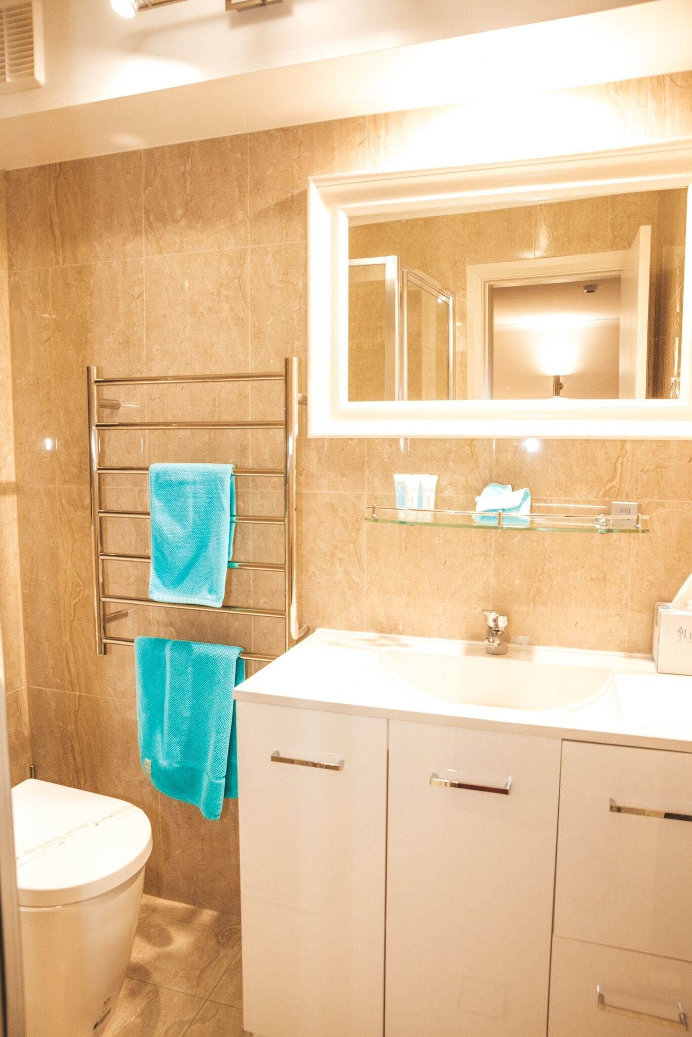 A bathroom with a toilet, a sink, a mirror, and a towel rack with two towels.