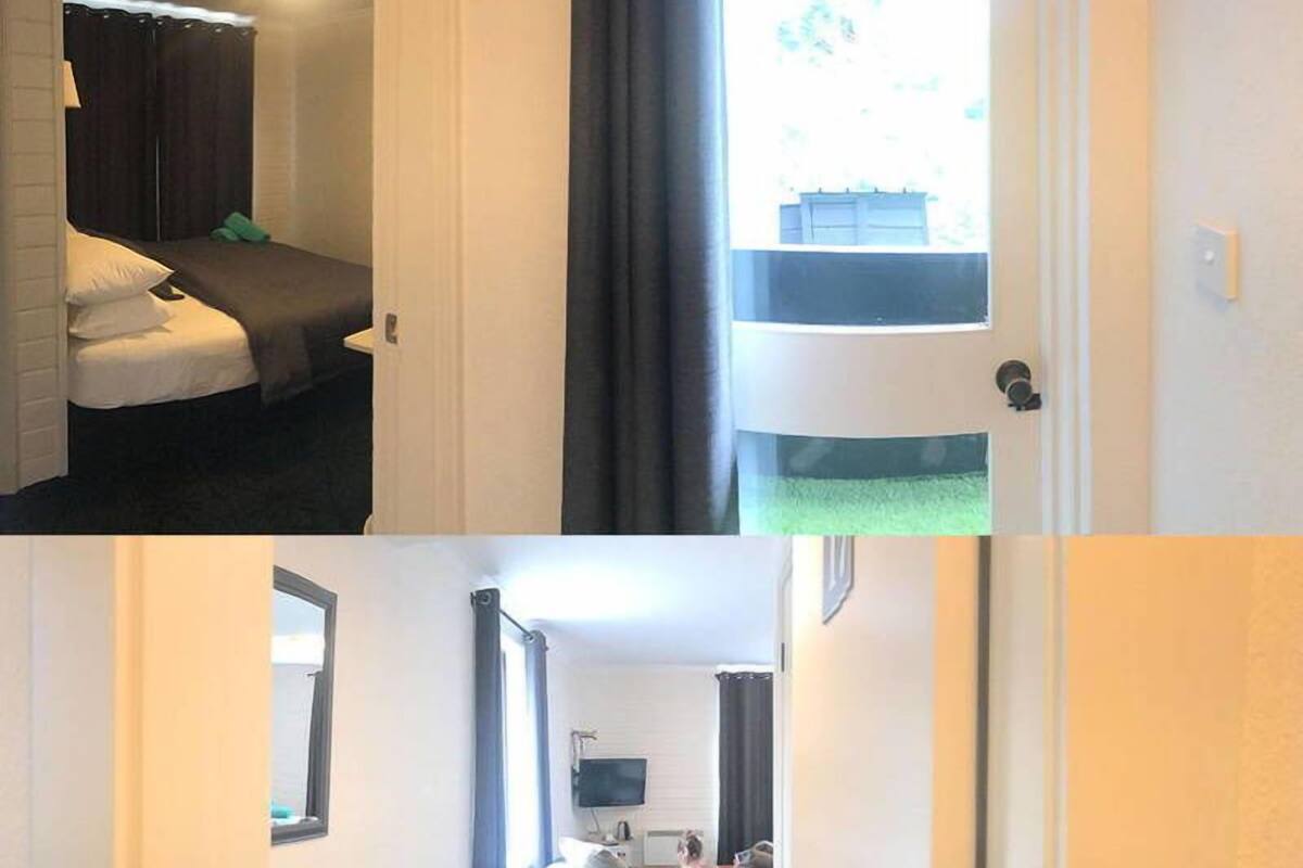 A hotel room with a bed, a window with curtains, a door, and a hallway leading to another room with a bed and a television.
