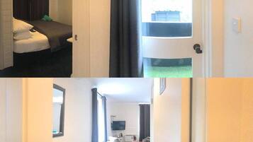 A hotel room with a bed, a window with curtains, a door, and a hallway leading to another room with a bed and a television.