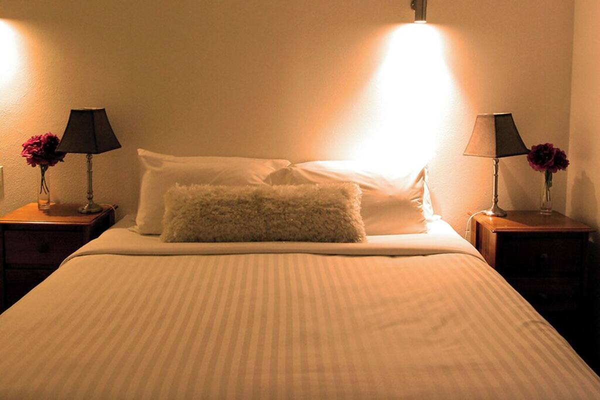 A neatly made bed with a fluffy pillow, two bedside lamps, and a vase with flowers on each nightstand.