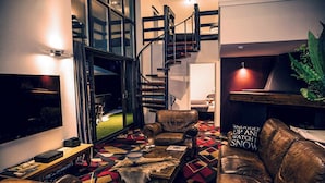 A modern living room with a geometric patterned floor, leather sofas, a staircase, and a television.