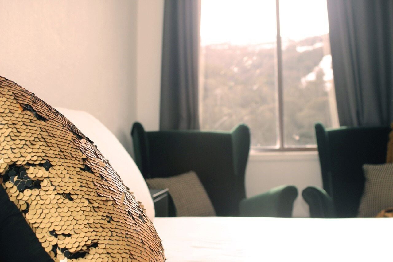 A bed with a patterned pillow, a window with curtains, and two chairs.