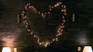A neatly made bed with a fluffy pillow, two bedside lamps, and a heart-shaped light decoration on the wall.