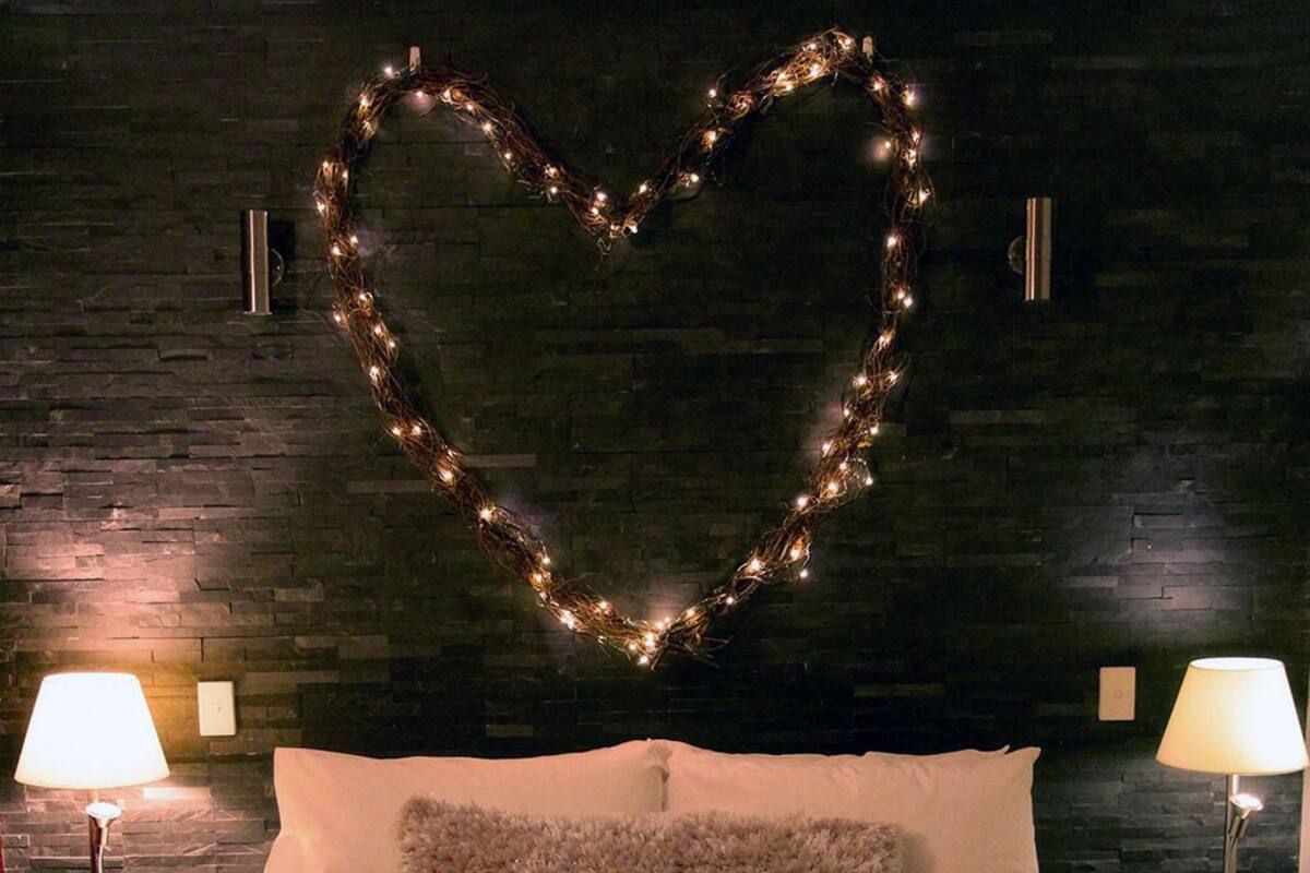 A neatly made bed with a fluffy pillow, two bedside lamps, and a heart-shaped light decoration on the wall.