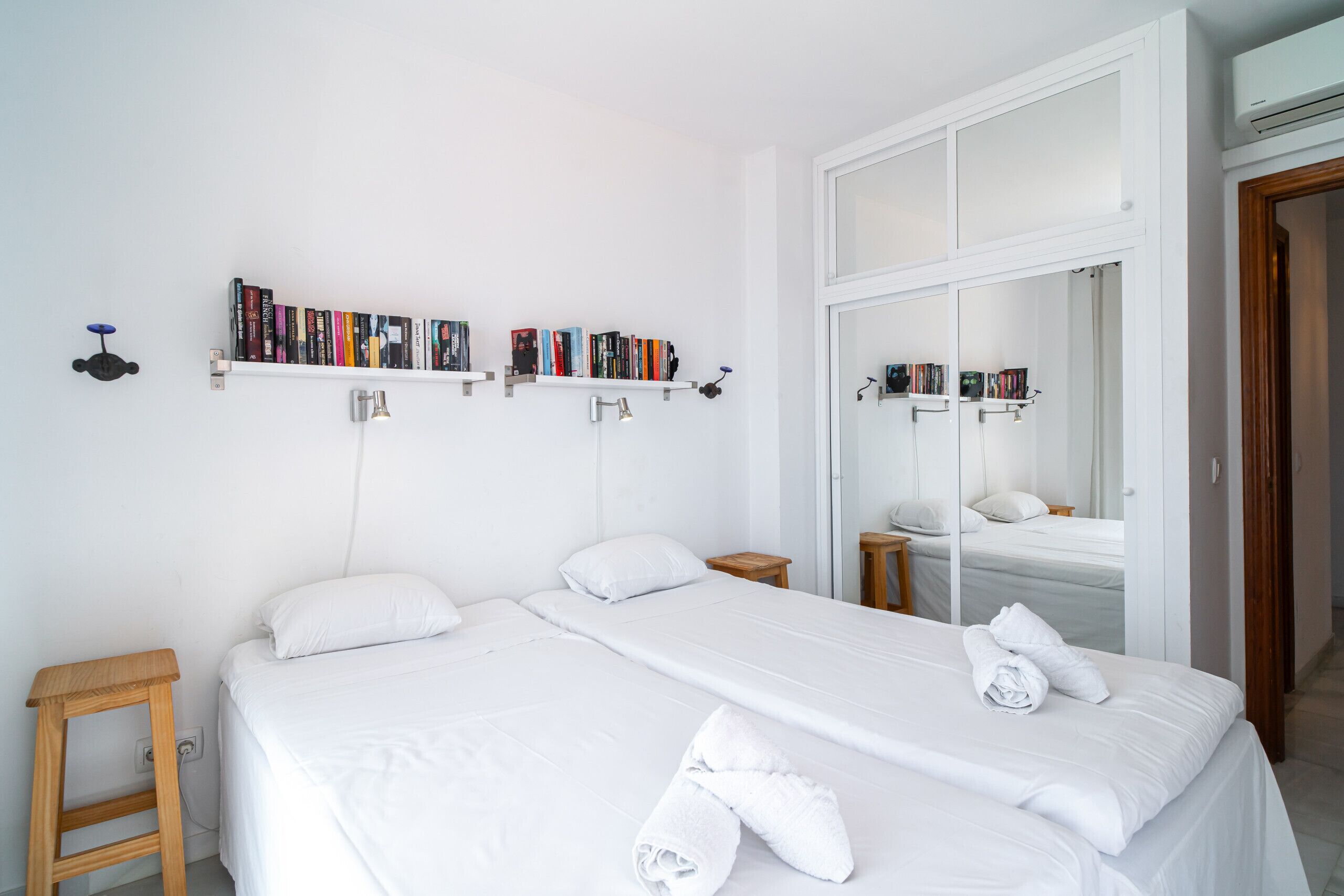 Quarto de hotel com duas camas, uma estante, um espelho e uma escada de madeira.