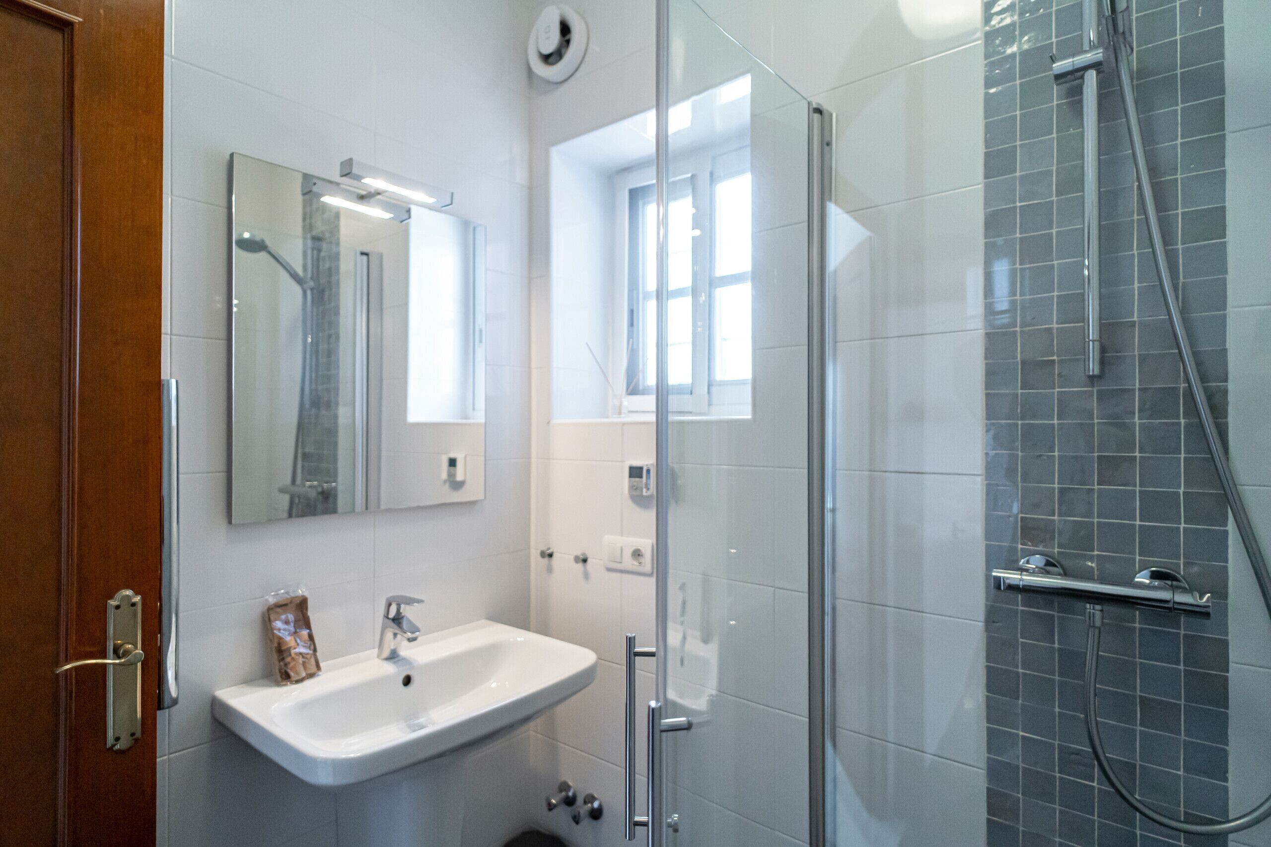 Un baño moderno con cabina de ducha de vidrio, un lavabo blanco y un espejo sobre él.