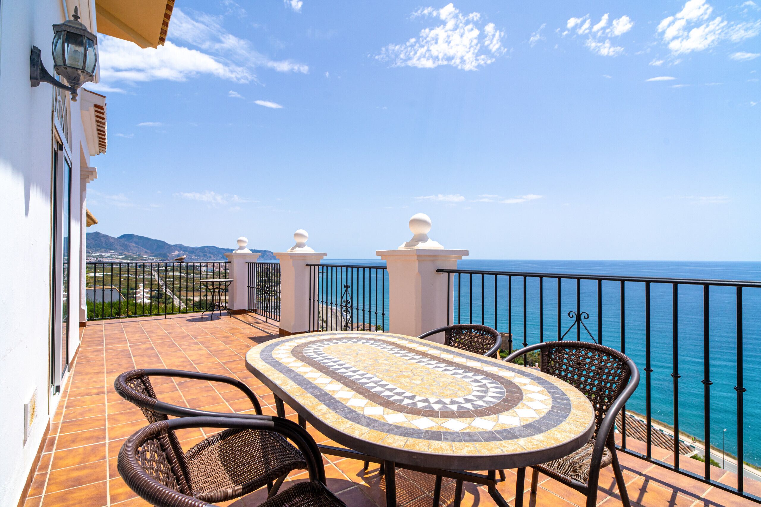Eine Terrasse mit gefliestem Tisch und Stühlen, einem Geländer und Blick auf das Meer.