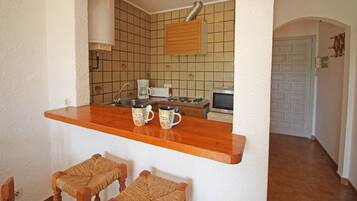 Een kleine keuken met een houten aanrecht, twee geweven stoelen en een betegelde spatwand.