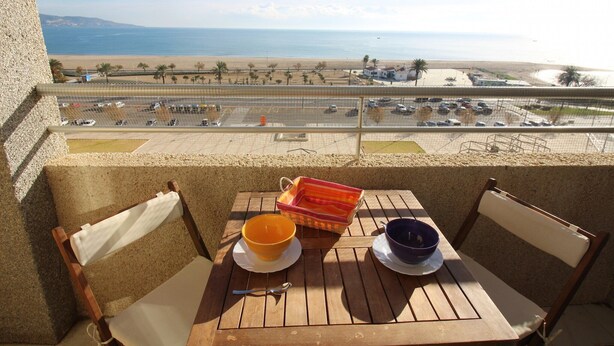 A balcony with a table and chairs overlooking a beach and parking area. - Studio in Empuriabrava with Sea Views (Empuriabrava)