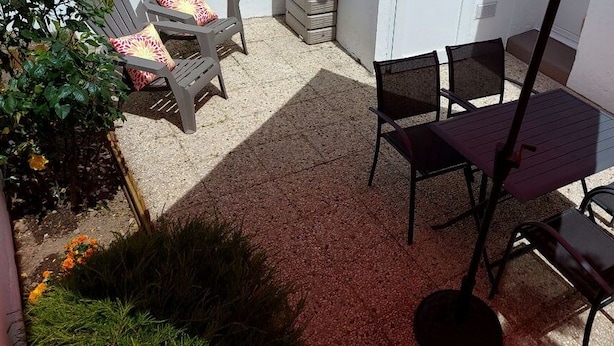 Un espace patio aménagé avec une table et des chaises, entouré de plantes et bordé d’un mur blanc.