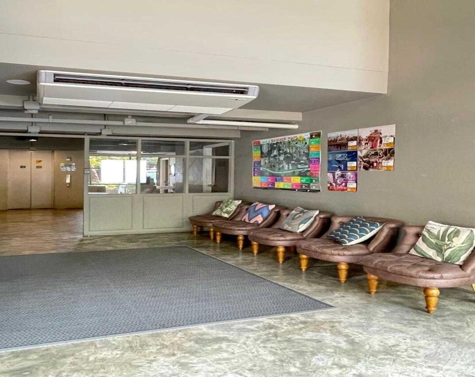 A lobby with a seating area, a large air conditioning unit, and a wall with various maps and pictures.