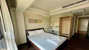 Une chambre d’hôtel avec un grand lit, un bureau, une chaise, une armoire et une salle de bain visible au fond.