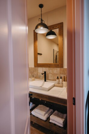 A modern bathroom with two sinks, a large mirror, and wooden shelves with towels.