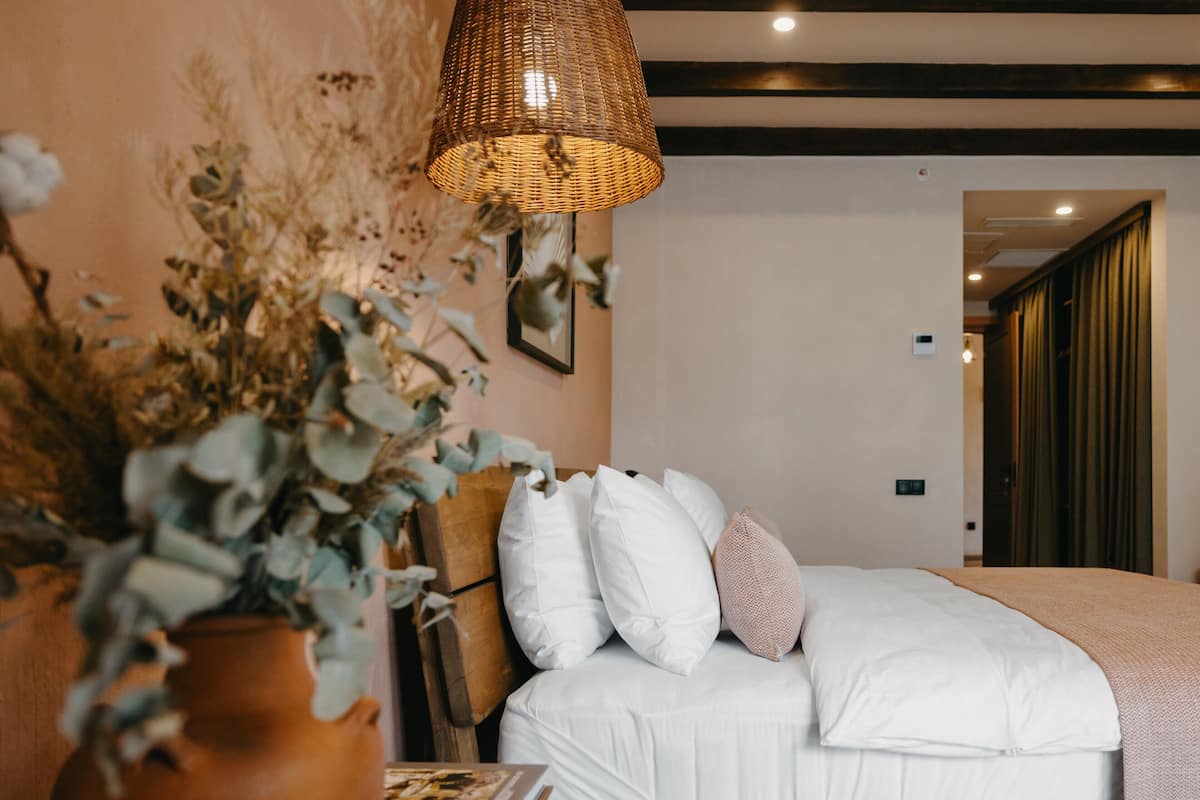 Ein Schlafzimmer mit einem Bett, Kissen, einer Vase mit getrockneten Blumen und einer Pendelleuchte.