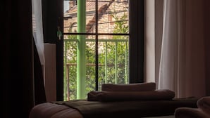 A room with a large window, a bed, and a view of a church with a bell tower. - Hameau Mukhrani (Mtskheta)