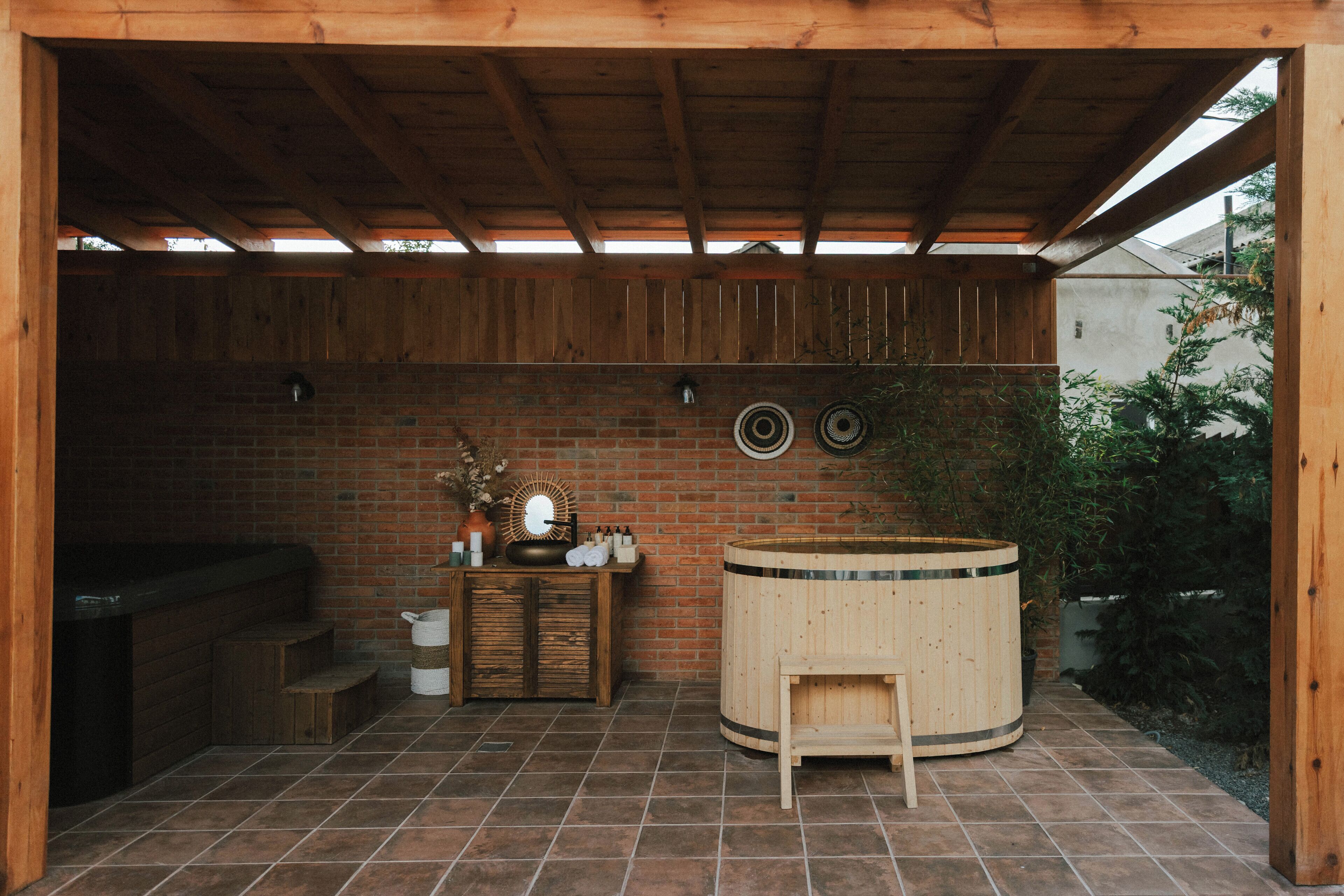 Un'area esterna coperta con un muro in mattoni, panche in legno, una vasca idromassaggio e un barbecue.
