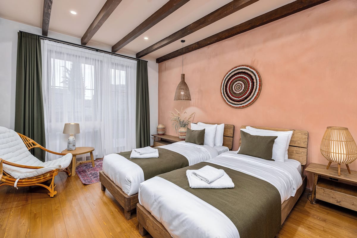 Ein Hotelzimmer mit zwei Betten, einem Holzstuhl, einem kleinen Tisch und einem Wandbild.