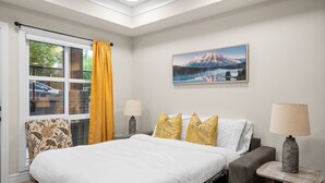 A bedroom with a bed, a chair, a table, a lamp, and a painting on the wall.