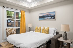 Quarto com cama, cadeira, mesa, abajur e um quadro na parede.