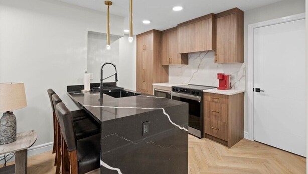 A modern kitchen with a central island, wooden cabinets, and a red coffee machine.