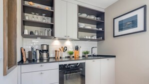 A modern kitchen with white cabinets, a built-in oven, and a countertop with various appliances and utensils.