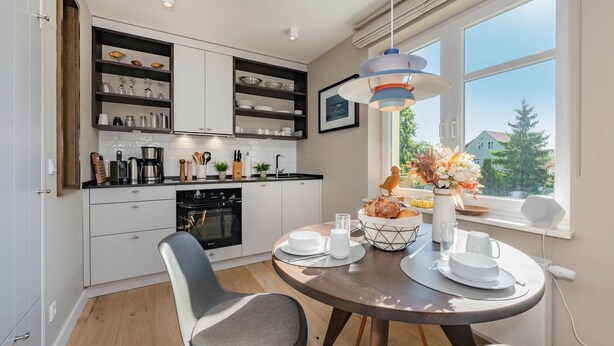 A modern kitchen with white cabinets, black countertops, and a dining area with a round table and two chairs.