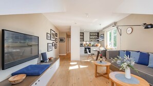 A modern living room with a large TV, wooden flooring, a sofa, and a dining area with a table and chairs.