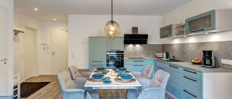Una cocina moderna con comedor, que presenta armarios azul claro, una mesa con cubierta de mármol y sillas tapizadas en gris.