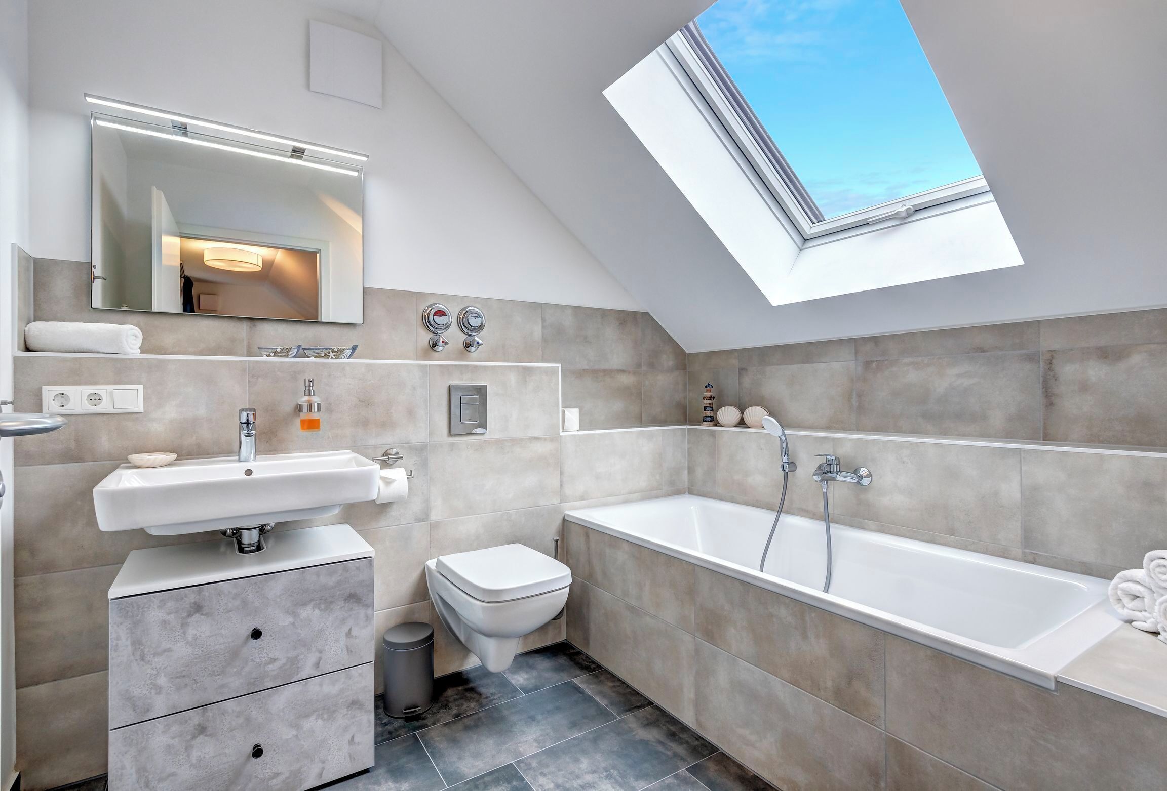 A modern bathroom with a skylight, a bathtub, a toilet, and a vanity with a mirror and sink.