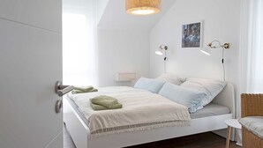 Une chambre moderne avec un lit, des lampes de chevet, un luminaire suspendu et une petite table.