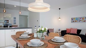 Un espace repas moderne avec une table en bois dressée pour quatre personnes, entourée de chaises en osier, et une cuisine en arrière-plan.