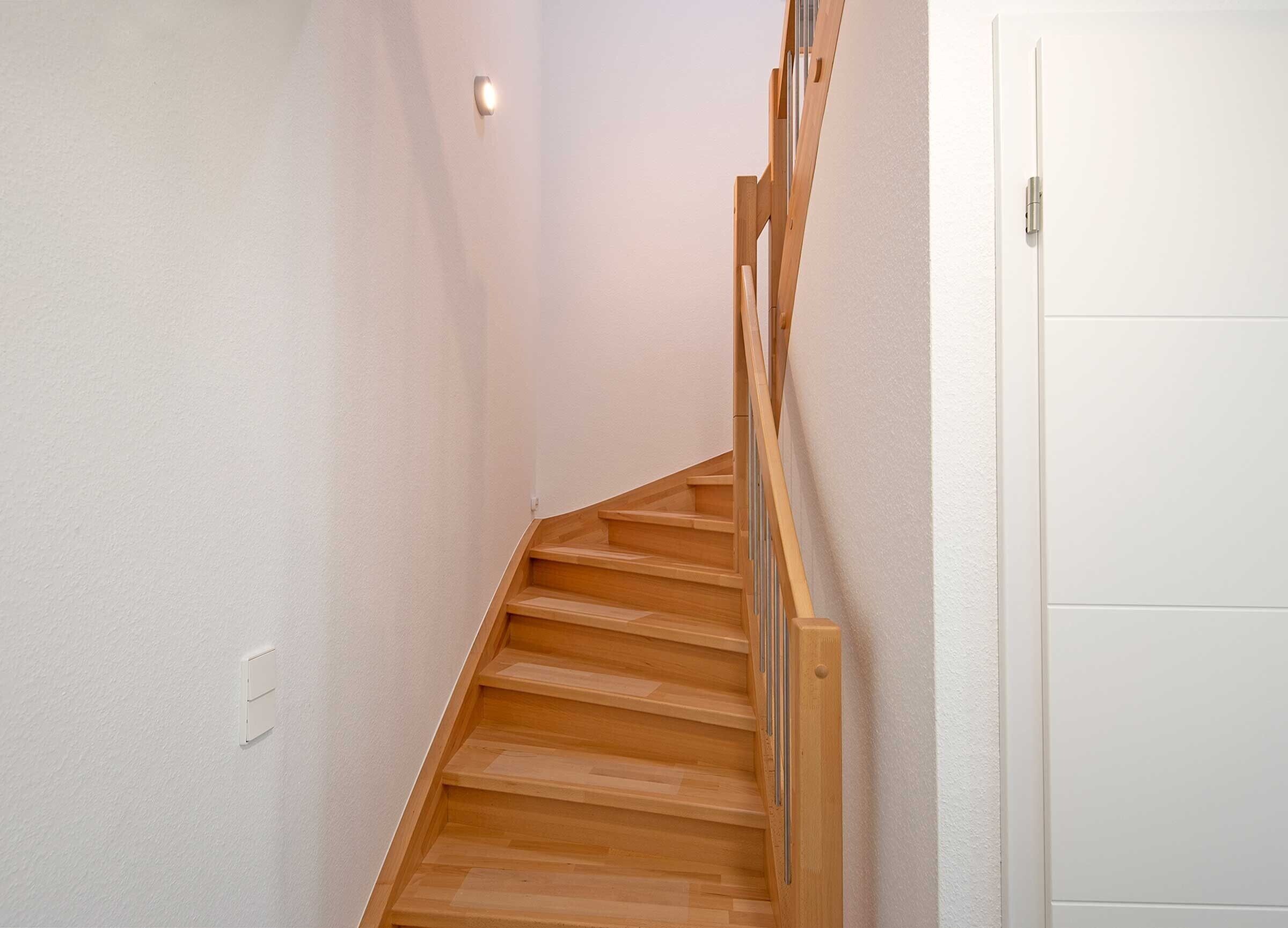 Un escalier en bois avec une rampe, des murs blancs et une porte en bas.