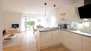 Une cuisine moderne avec des meubles blancs, un grand îlot central, des luminaires suspendus et un téléviseur.