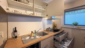 A compact kitchen with a wooden countertop, built-in shelves, a window with blinds, and a small potted plant. - Casa Limone - Exclusive relaxation by the Baltic Sea - stylish living in Scharbeutz (Scharbeutz)
