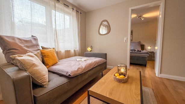 A cozy living room with a sofa, a small table with a candle, and a view into another room. - Casa Limone - Exclusive relaxation by the Baltic Sea - stylish living in Scharbeutz (Scharbeutz)