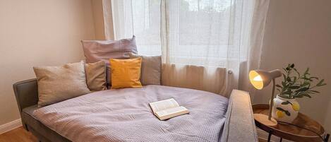 Une chambre à coucher bien rangée, avec un lit, des oreillers, une table de chevet avec une lampe et une petite plante.
