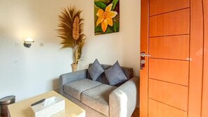 A room with a grey sofa, a wooden table with a tissue box, a potted plant, and a wooden door. - Abams Gili Air (Gili Air)
