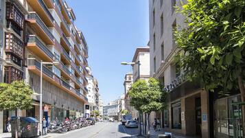 Een straat met hoge gebouwen, waarvan sommige balkons hebben. Parkeermotoren en auto's staan langs de straat.