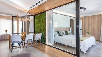 Een moderne hotelkamer met een grote schuifglazen deur naar een balkon, een bed met een witte dekbedovertrek, een tafeltje met een vaas, en een zithoek met stoelen en een klein tafeltje.