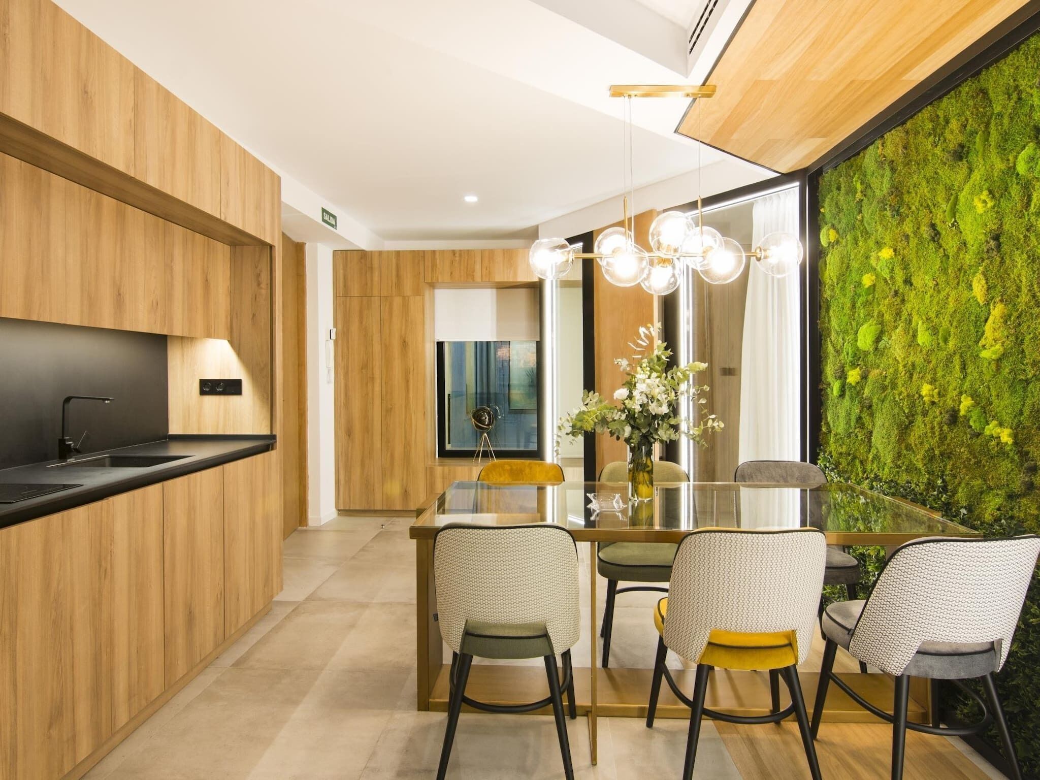 Une cuisine moderne avec des meubles en bois, un plan de travail noir et un coin repas comprenant une table et des chaises en verre.