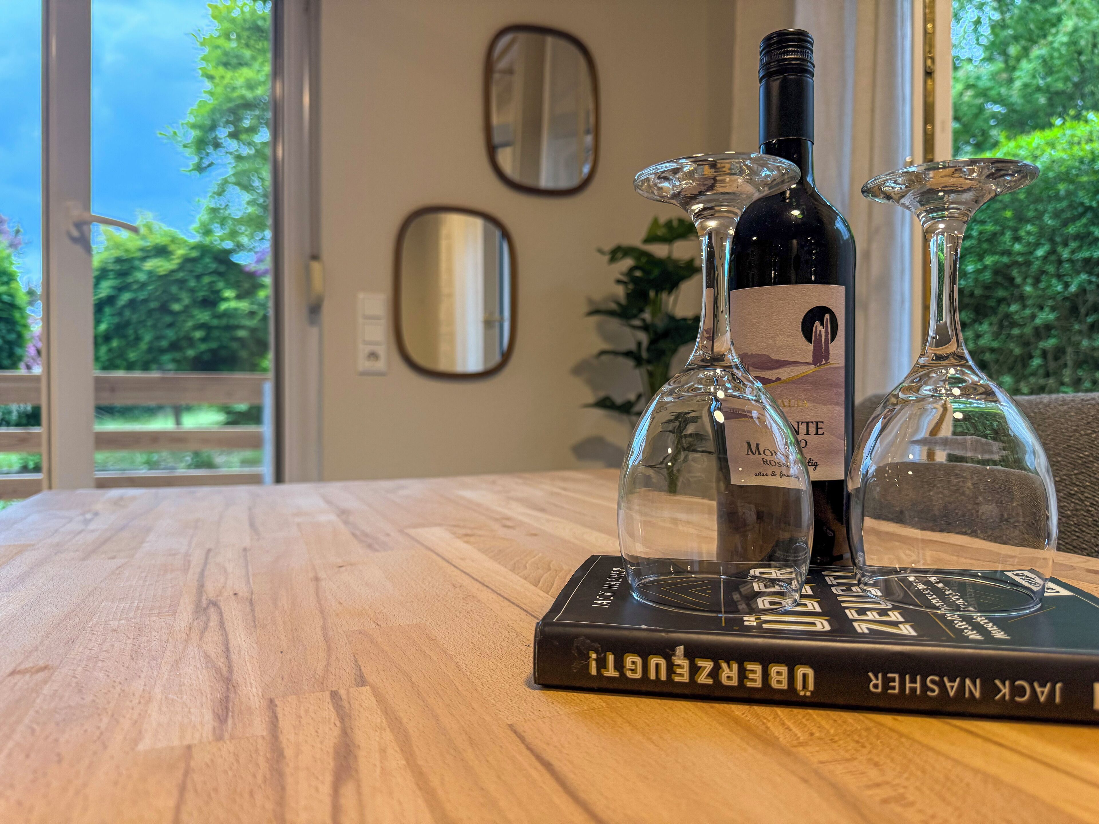 Une table en bois sur laquelle sont posés une bouteille de vin et deux verres à vin, le tout sur un livre intitulé « Jack Nasser ».