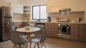 A modern kitchen with a stainless steel refrigerator, a built-in oven, and a coffee maker. There is a dining table with four chairs and a potted plant on the windowsill. - w* | Well-Located 2BR in Miraflores (Miraflores)