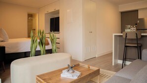 A modern hotel room with a bed, a wooden coffee table with books, a sofa, a kitchen area, and a bathroom visible through an open door. - w* |  Radiant 1BR w/ Private Balcony in Miraflores (Miraflores)