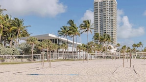Une plage avec un hôtel de grande hauteur, des palmiers et un filet de volley-ball.