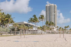A beach with a high-rise hotel, palm trees, and a volleyball net.
