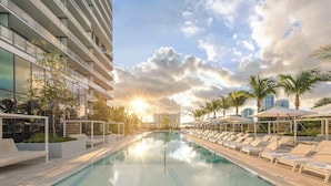 Un hôtel moderne doté d’une piscine, de chaises longues et de palmiers.