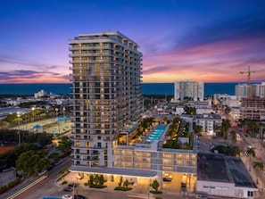A high-rise hotel with multiple balconies, a rooftop pool, and a view of the cityscape at dusk.